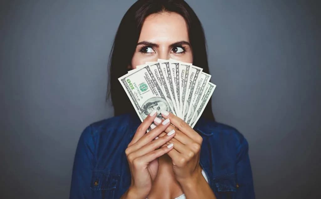 woman holding money - How To Save Money On Business Travel